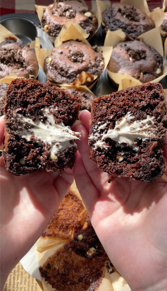An Oreo cookies and cream muffin cut in half, showing the moist chocolate crumb and the gooey white chocolate spread filling in the centre
